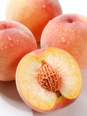 Целе и исечене брескве на дрвеном столу, поред чаше сока од брескве